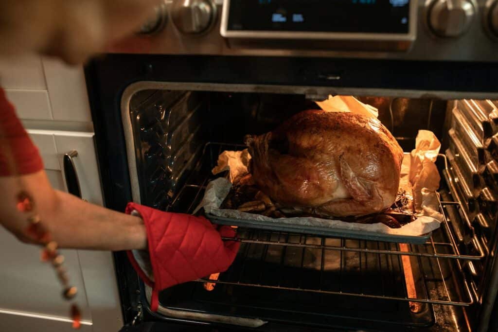 Golden roasted turkey being taken out of the oven, perfect for Thanksgiving dinner imagery.